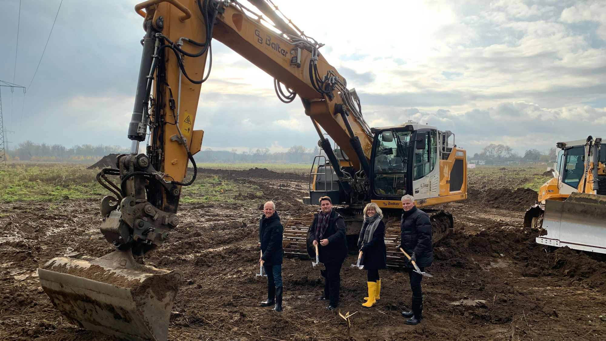 Vor einem Bagger stehen mit Spaten der Technische Beigeordnete der Stadt Troisdorf, Walter Schaaf, Bürgermeister Alexander Biber sowie die Geschäftführung der TroiKomm Andrea Vogt und Michael Roelofs.
