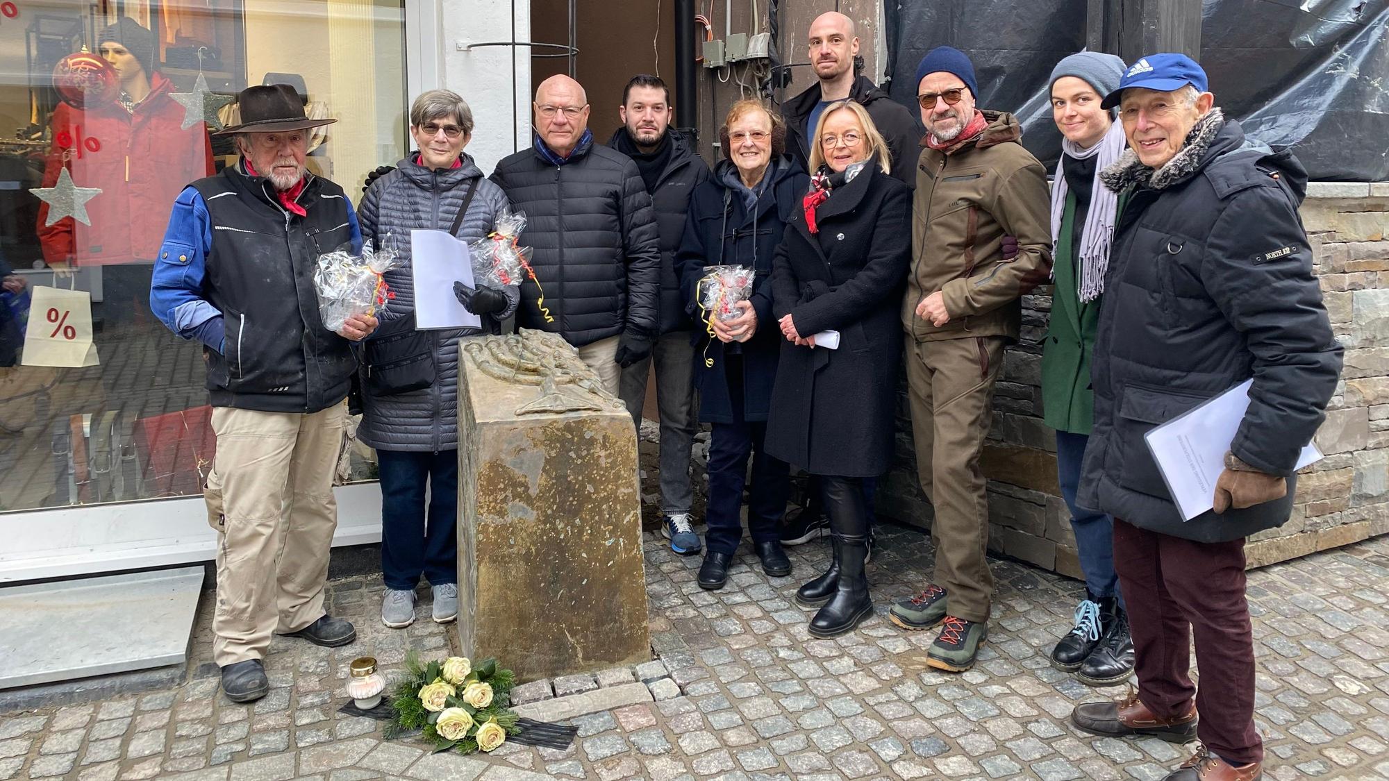 Künstler Gunter Demnig (l.) steht neben der Stele vor dem früheren Synagogenstandort in Bad Münstereifel. An ihrem Fuß sind weiße Rosen abgelegt. Unter den Teilnehmern der Aktion ist auch die Bad Münstereifeler Bürgermeisterin Sabine Preiser-Marian (4.v.r.).