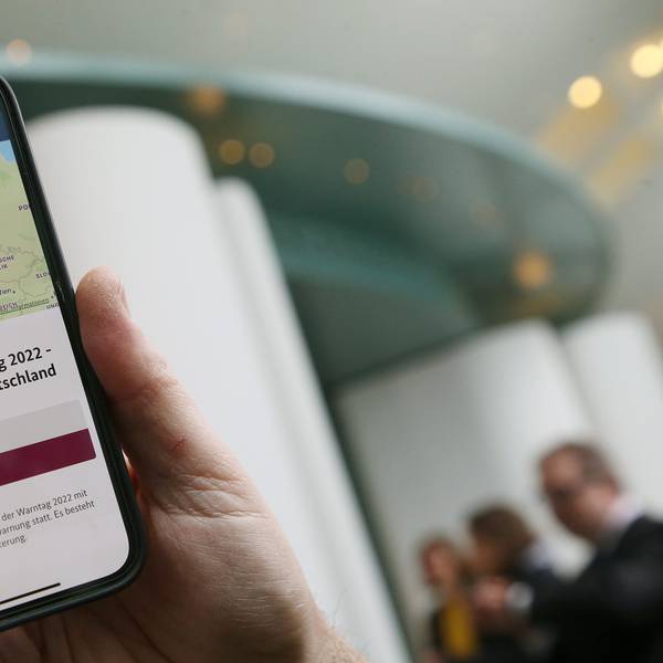 Ein Mitarbeiter des Bundeskanzleramts hält sein Mobiltelefon am Warntag 2022 im Foyer des Kanzleramtes in der Hand, wobei auf dem Display eine Probe-Warnmeldung zu sehen ist.