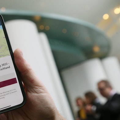 Ein Mitarbeiter des Bundeskanzleramts hält sein Mobiltelefon am Warntag 2022 im Foyer des Kanzleramtes in der Hand, wobei auf dem Display eine Probe-Warnmeldung zu sehen ist.