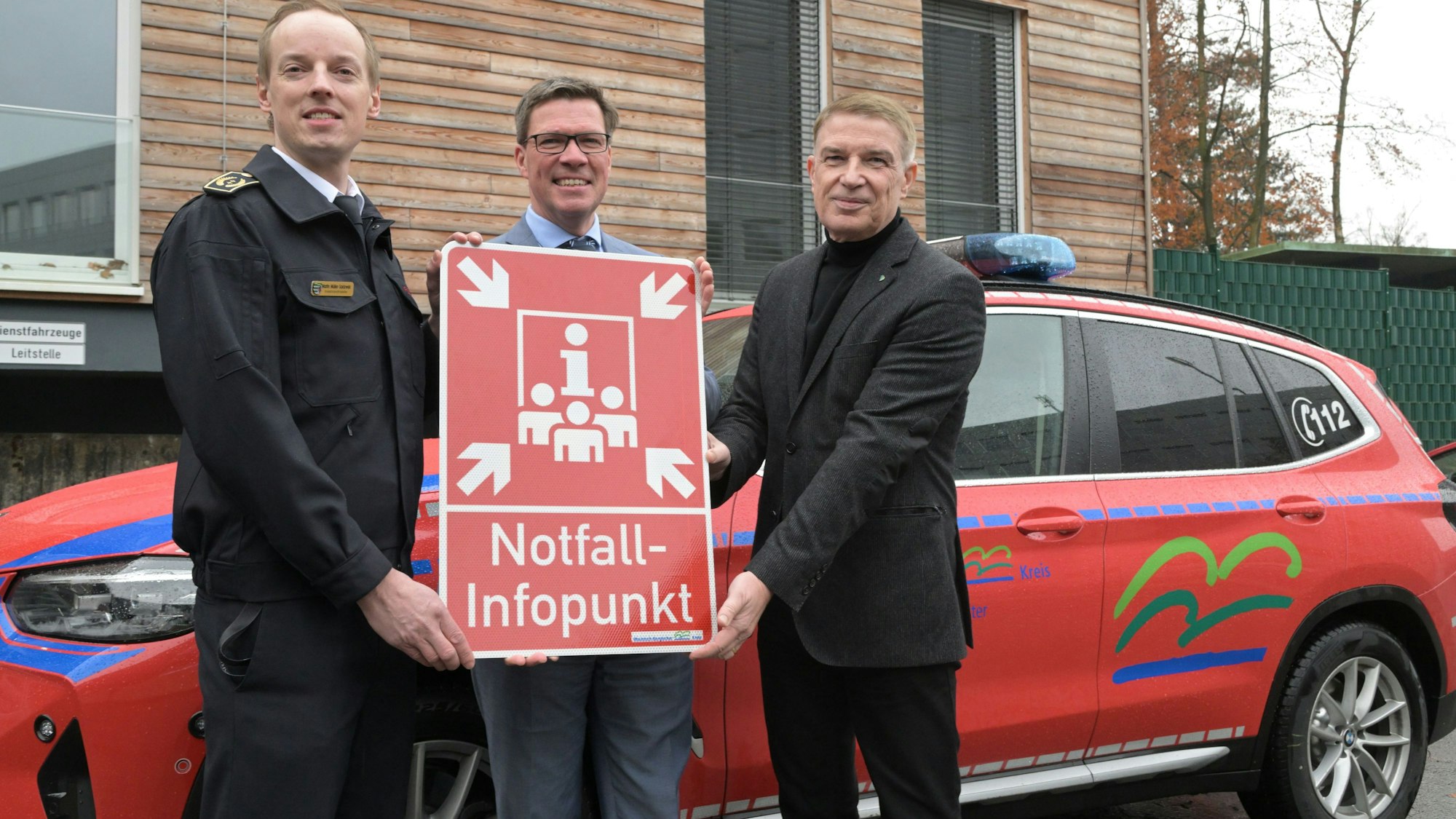 Kreisbrandmeister Martin Müller- Saidowski, Landrat Stephan Santelmann, und Kreisdirektor Dr. Erik Werdel stehen vor einem roten Wagen und halten ein rotes Hinweisschild auf einen NIP in den Händen.