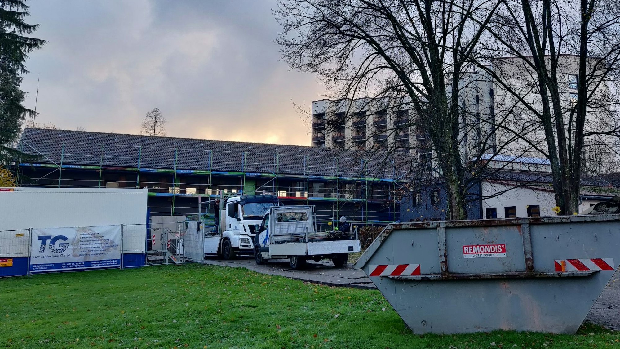 Schuttcontainer und Lastwagen stehen vor dem eingerüsteten Altbau des alten Badehauses neben dem Hochhaus der Klinik Roderbirken, das abgebrochen wird.