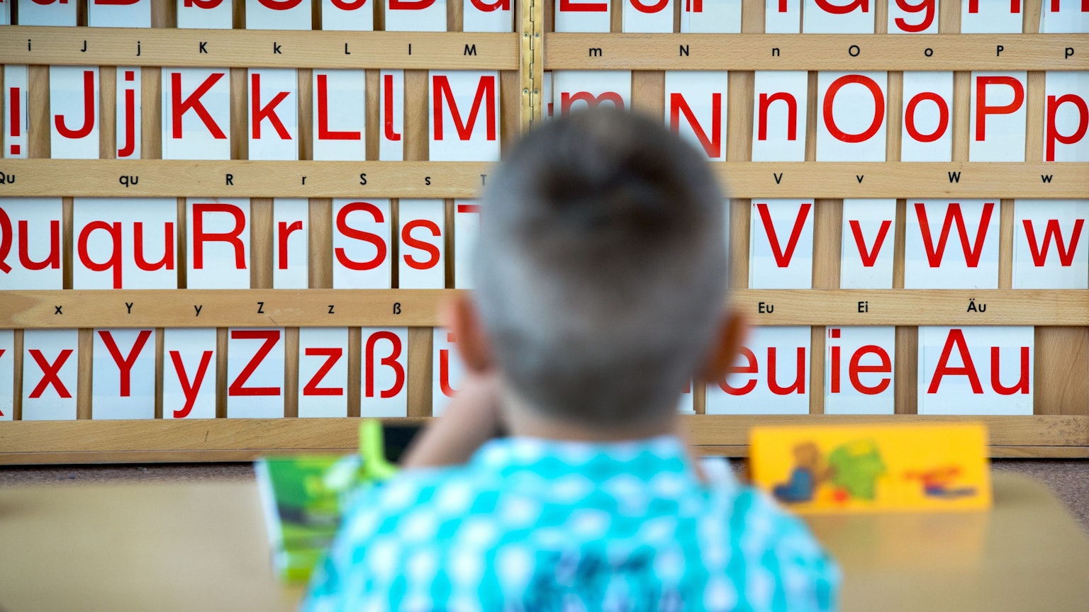 Ein Kind sitzt vor einer Tafel mit Buchstaben.