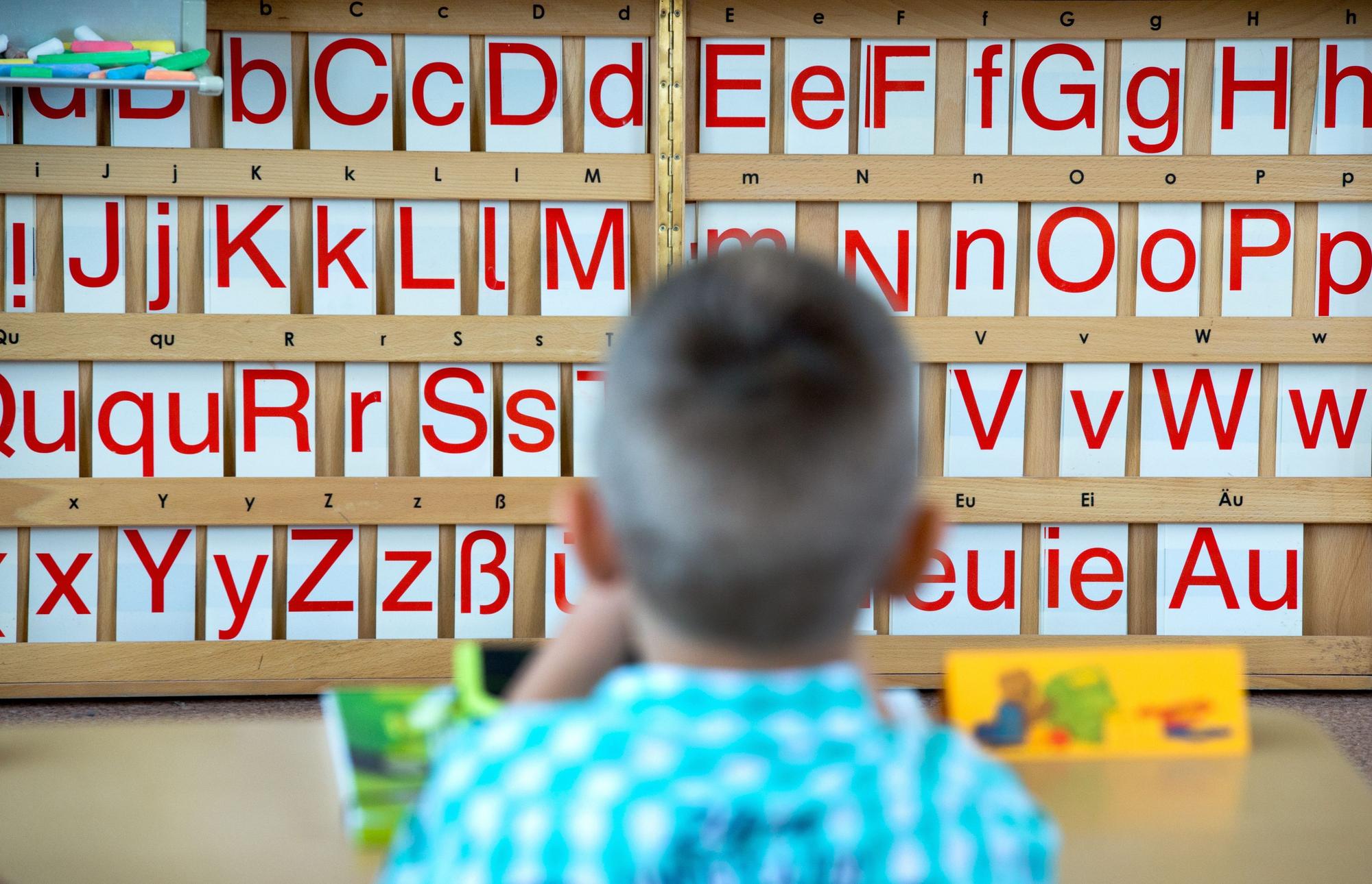 Ein Kind sitzt vor einer Tafel mit Buchstaben.