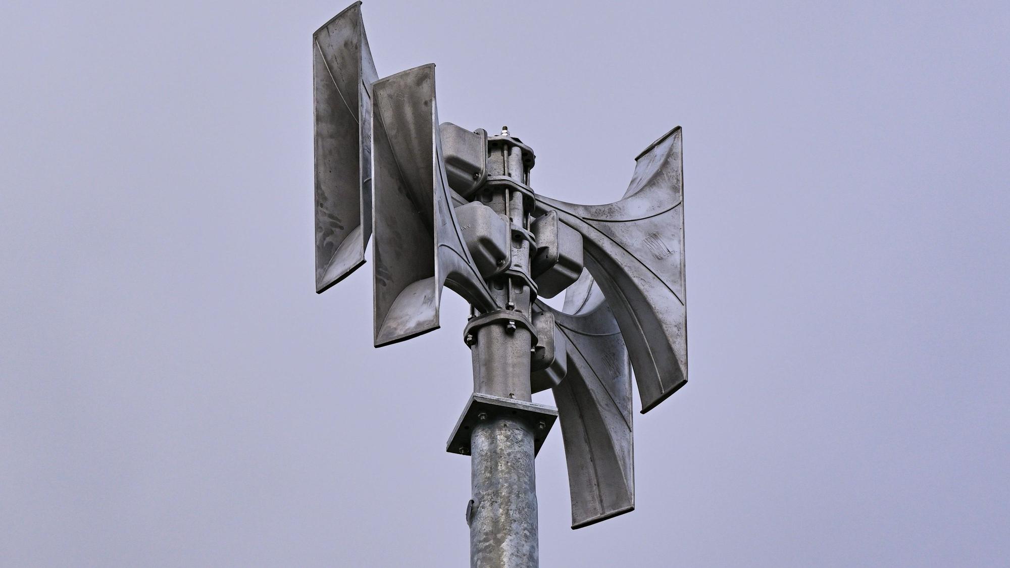 Eine Sirene aus Metall vor blauem Himmel.