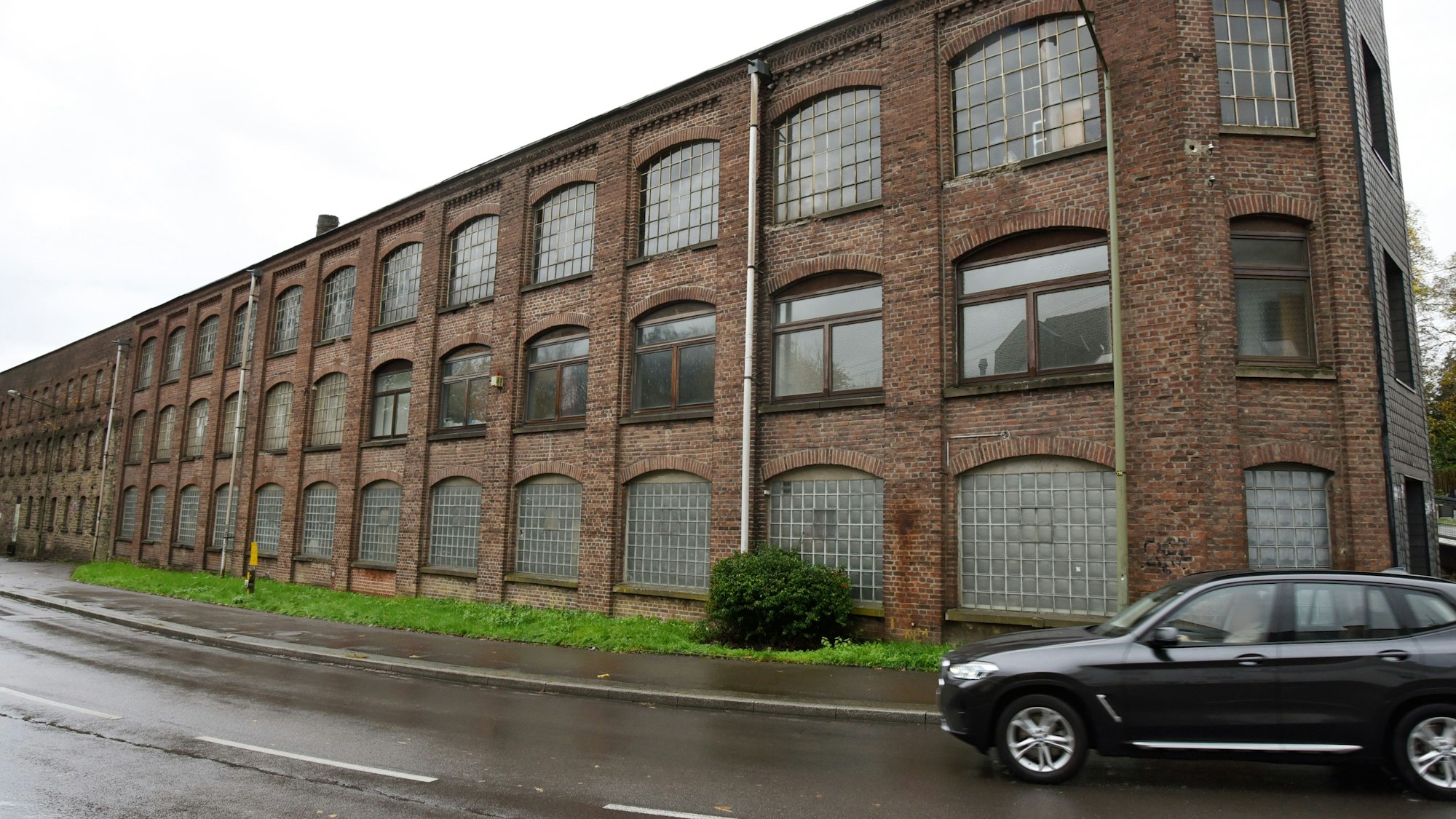 Auf regennasser Fahrbahn fährt ein schwarzer Pkw an der Alten Bücherfabrik Jaeger in Ründeroth vorbei. Was aus der Industriebrache werden soll, ist nach wie vor unklar. Ein Bürgerbegehren möchte erreichen, dass die Gemeinde sich doch um weitere Fördergelder bemüht.