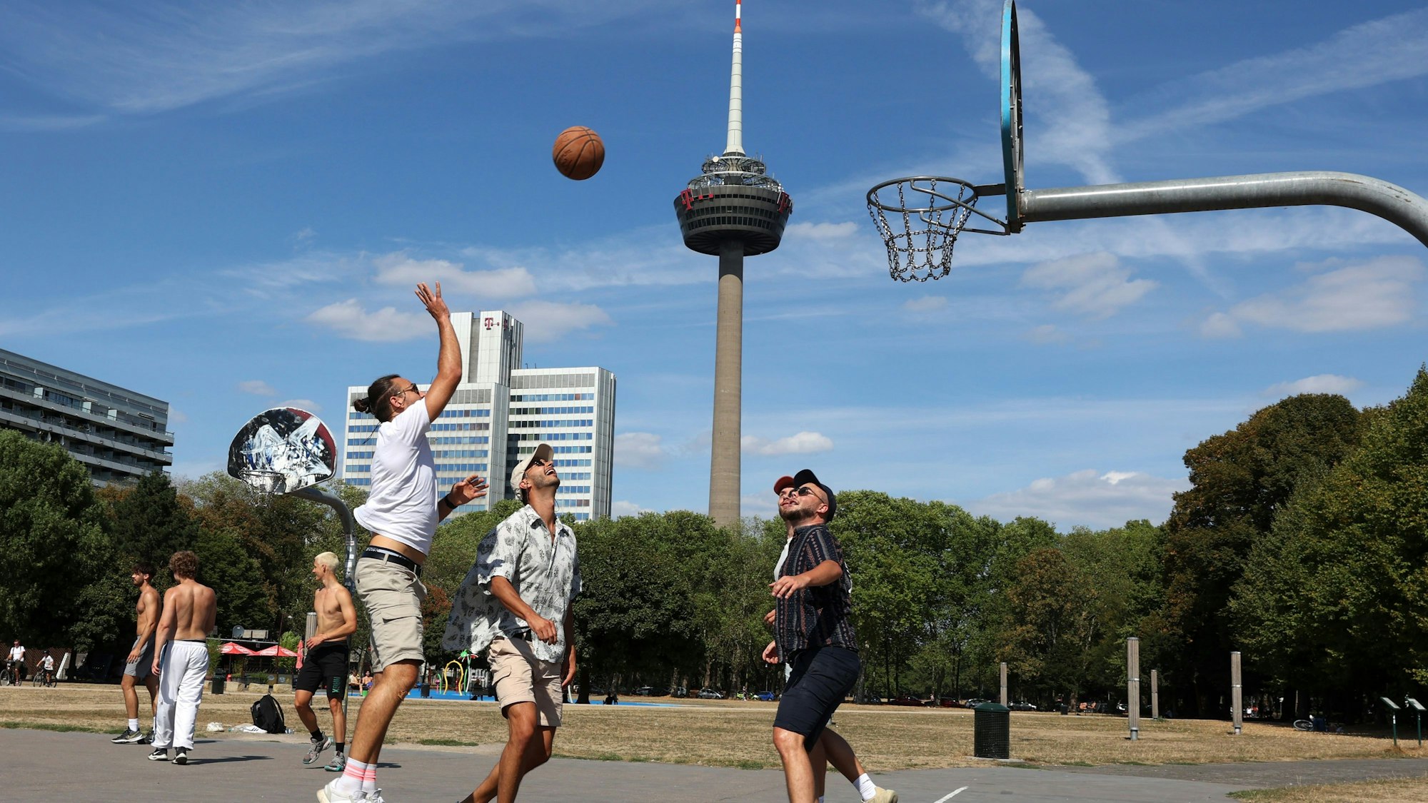 Mehrere junge Männer spielen Basketball auf einem Basketballplatz am Grüngürtel.