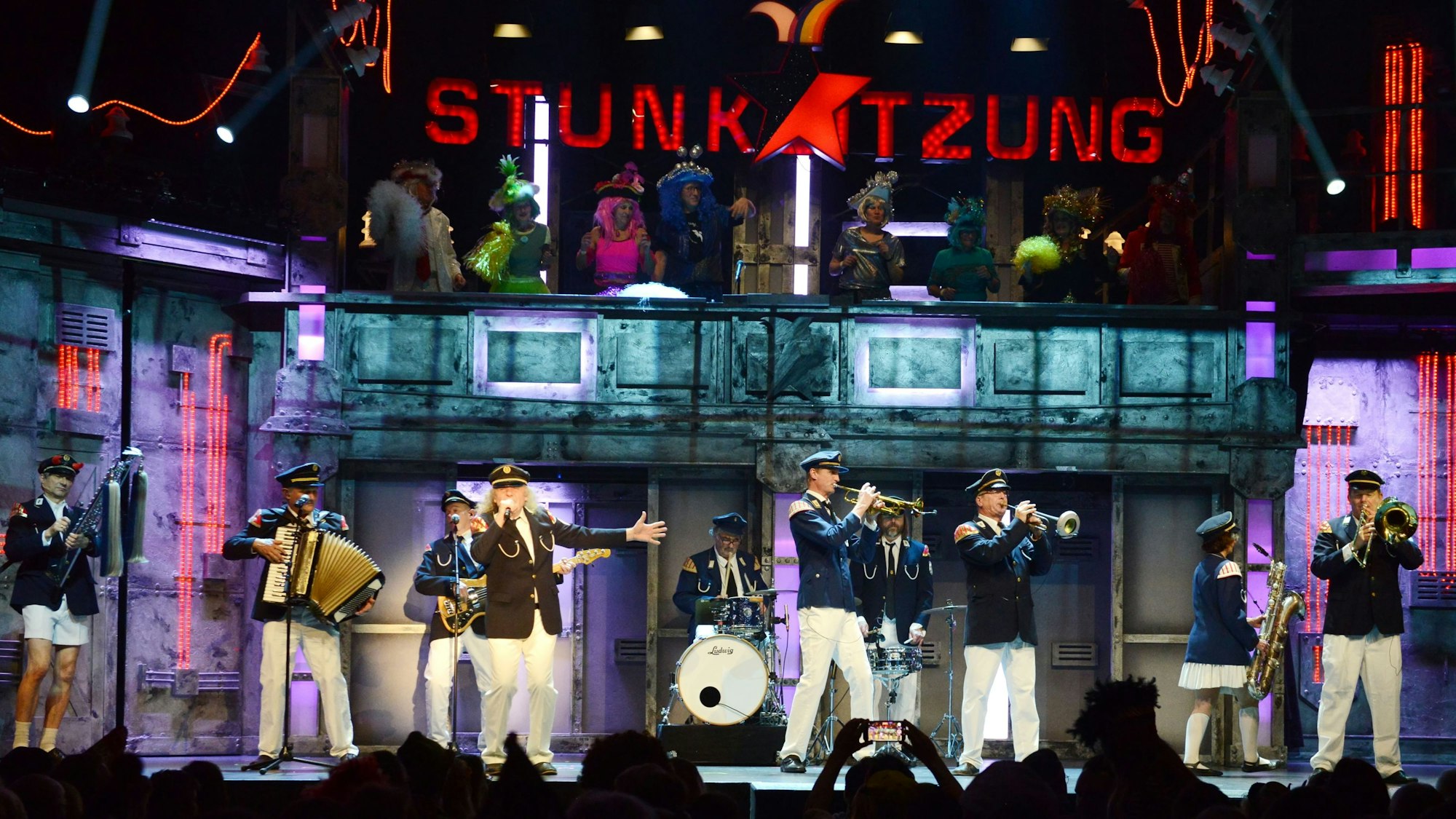 Das „Tanzkorps Heisterbacher Rott“ übt für das Metal-Festival in Wacken, einer der zahlreichen starken Auftritte der Hausband Köbes Underground. Im Hintergrund das Logo der Stunksitzung über dem Elferrat.