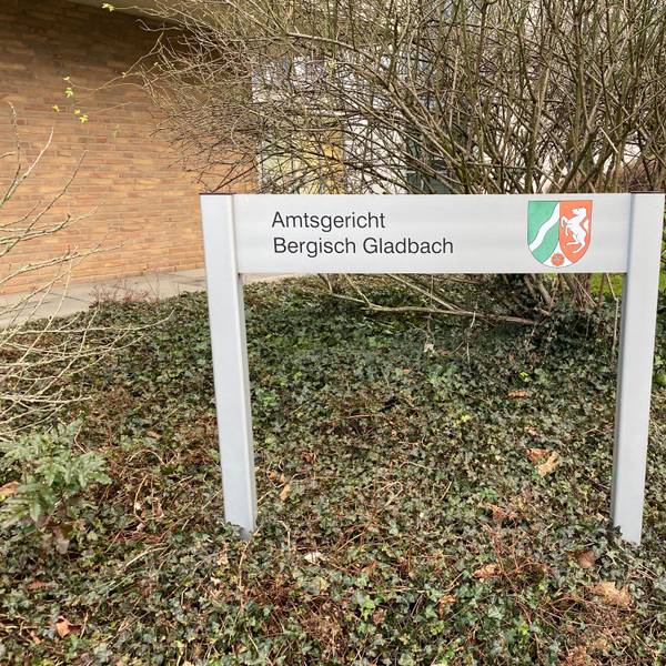 Vor dem Amtsgericht steht ein Schild mit der Aufschrift Amtsgericht Bergisch Gladbach.