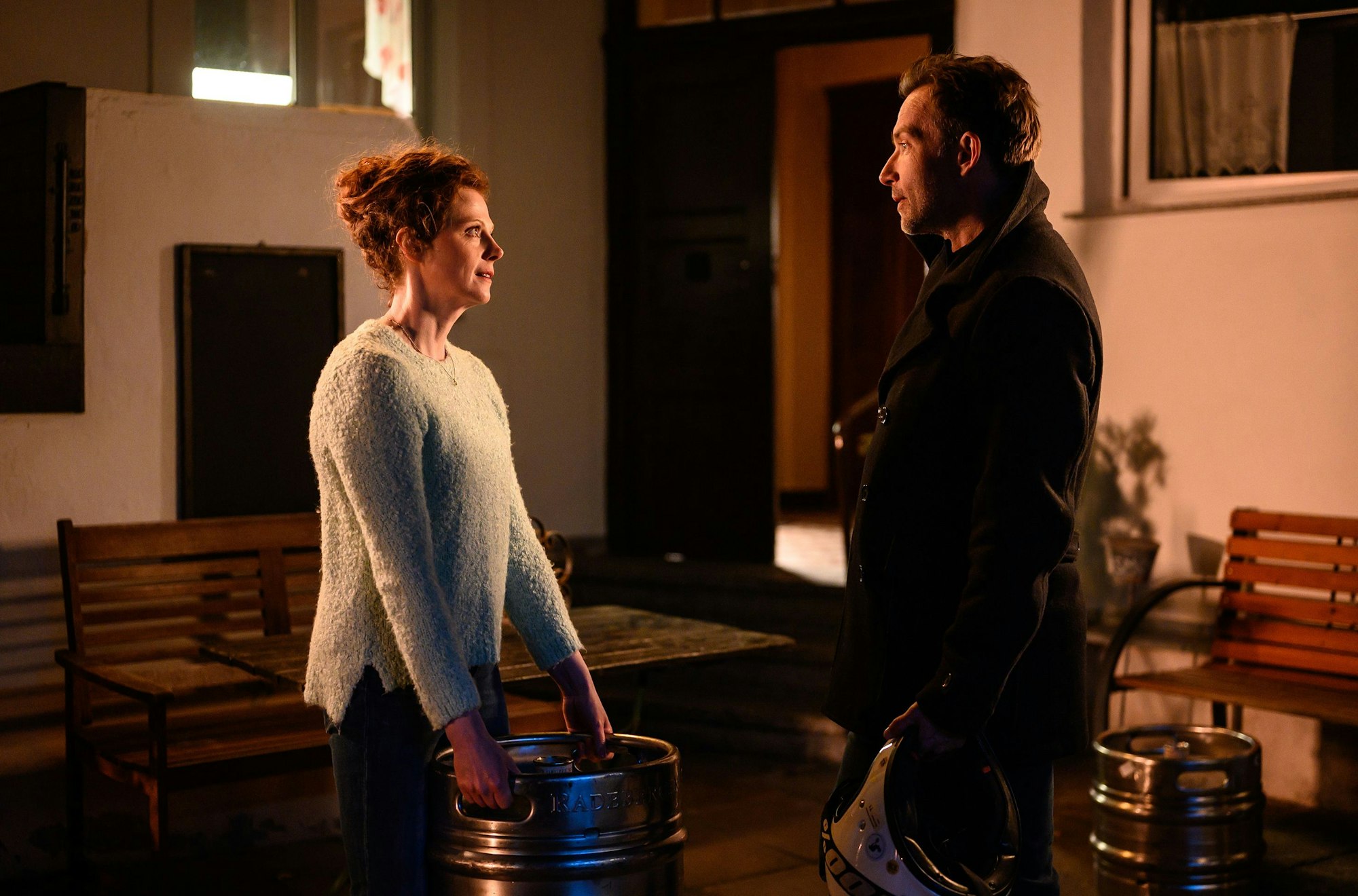 Eva Wozniak trägt ein schwered Bierfass, ihm gegenüber steht Adam Raczek und bietet ihr seine Hilfe an.