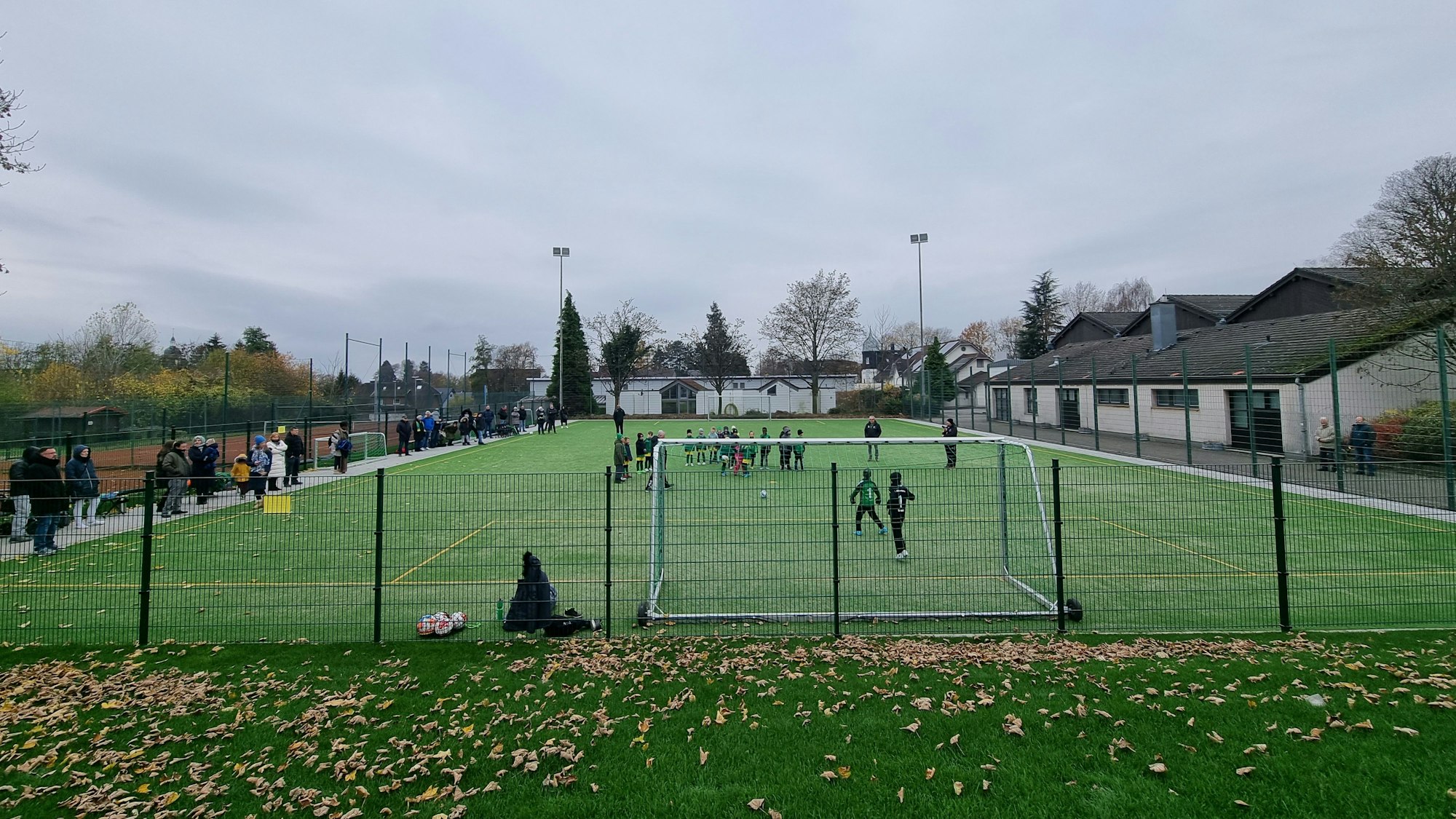 Blick von einer erhöhten Position auf das kleine Kunstrasenfeld des BV Bergisch Neukirchen. Kinder spielen darauf Fußball.