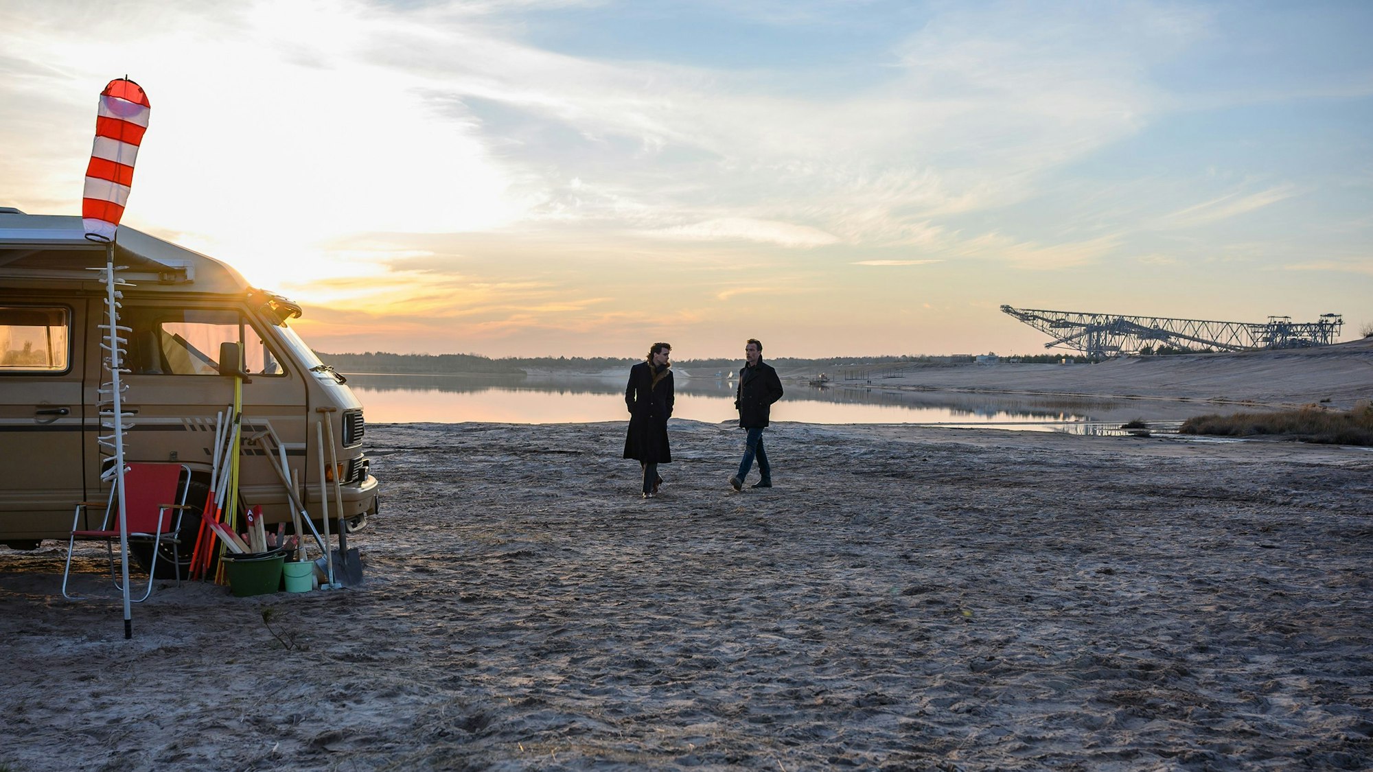 Ein weiter Ausblicam Strand eines Sees, im Hintergrund der ehemalige Tagebau. Links der Camper der Getöteten, in der Mitte das Ermittlerduo.