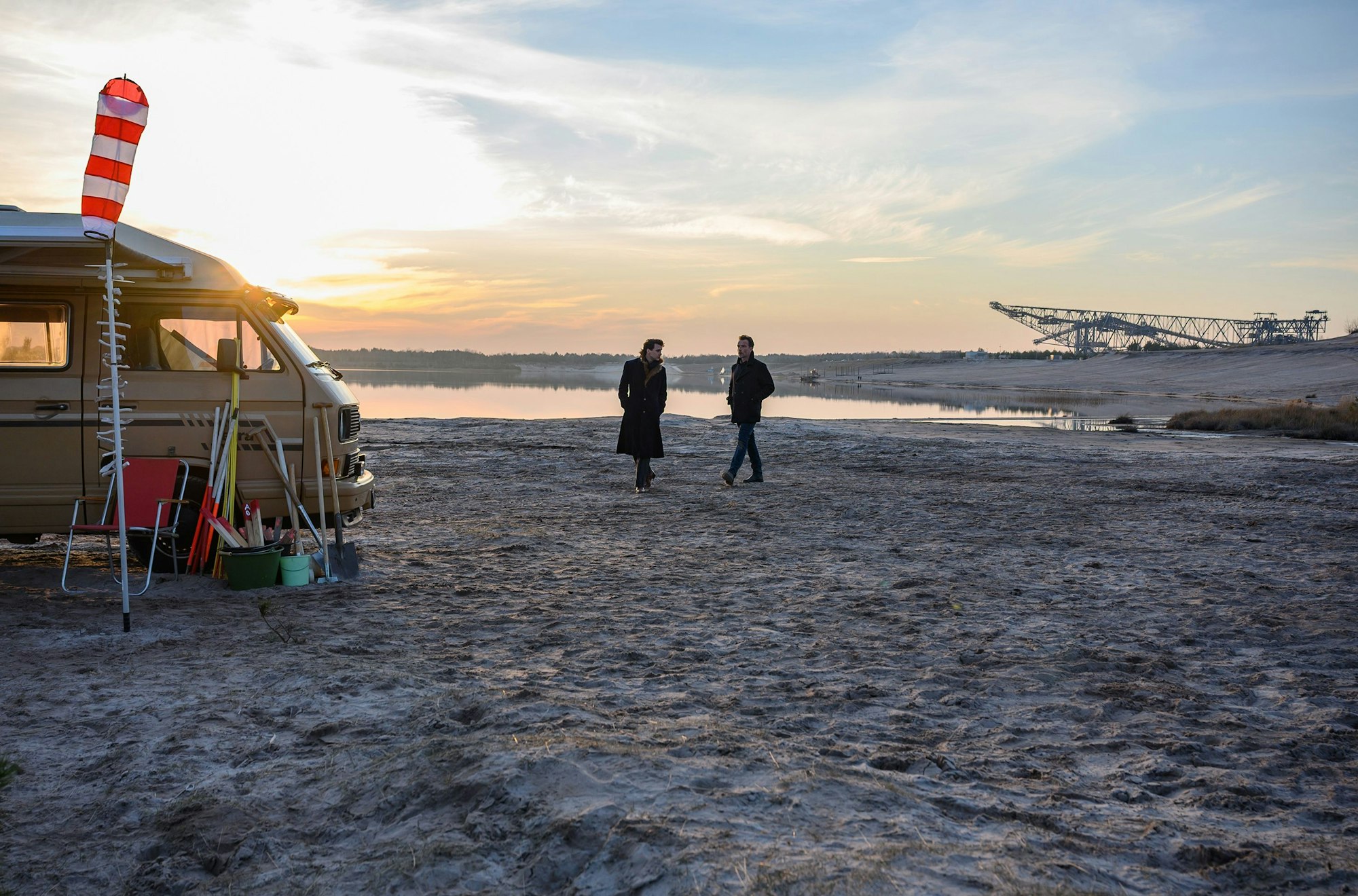 Ein weiter Ausblicam Strand eines Sees, im Hintergrund der ehemalige Tagebau. Links der Camper der Getöteten, in der Mitte das Ermittlerduo.