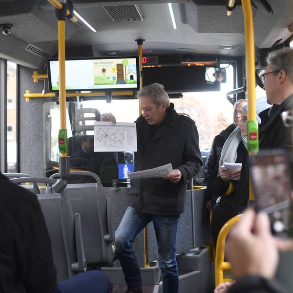 Andreas Glodowski steht in einem Kleinbus und hält einen ausgedruckten Fahrplan hoch, während er das neue Zülpicher ÖPNV-Konzept vorstellt.