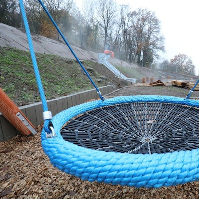 Eine große runde Schaukel steht neben dem Gebäude einer Kita.