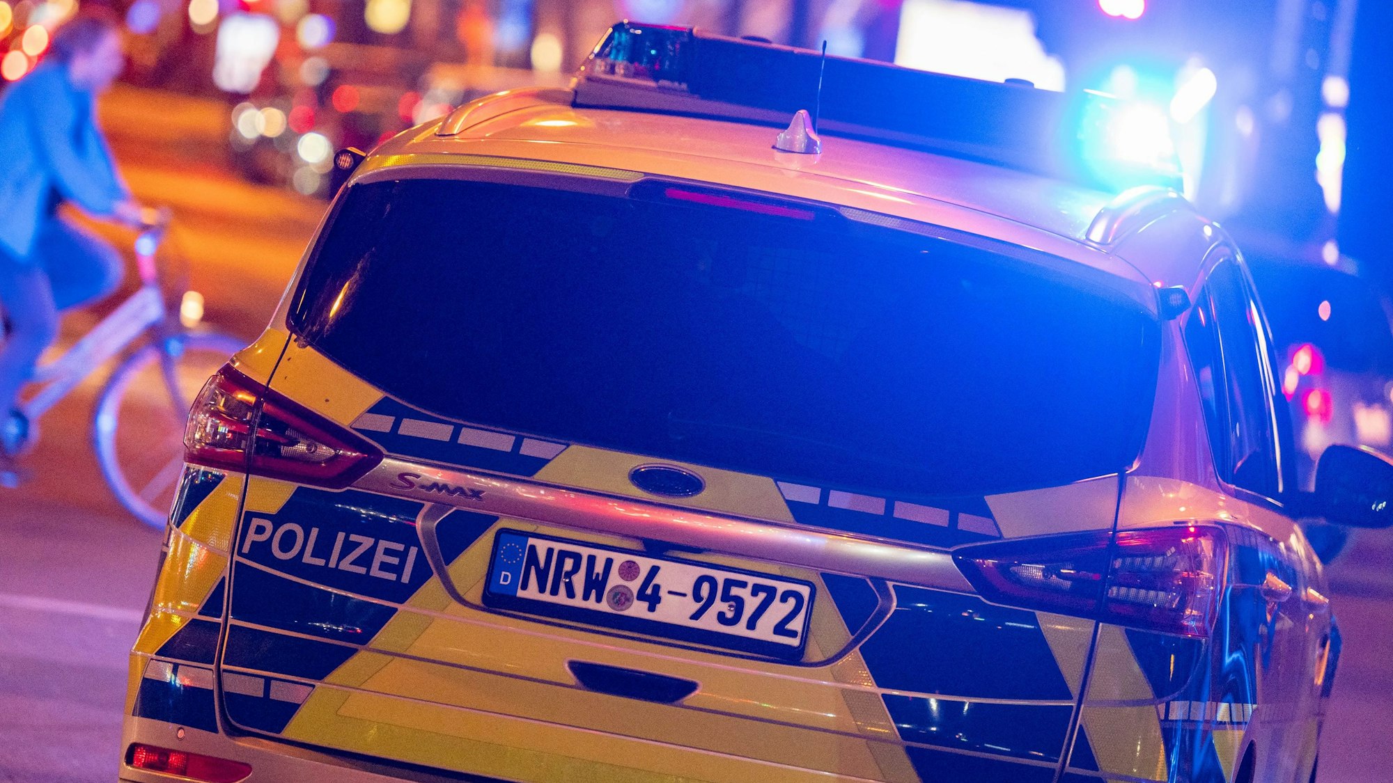 Ein Polizei-Auto in blau-gelber Lackierung fährt über eine Straße in Köln, es ist mit Blaulicht unterwegs. (Symbolbild)