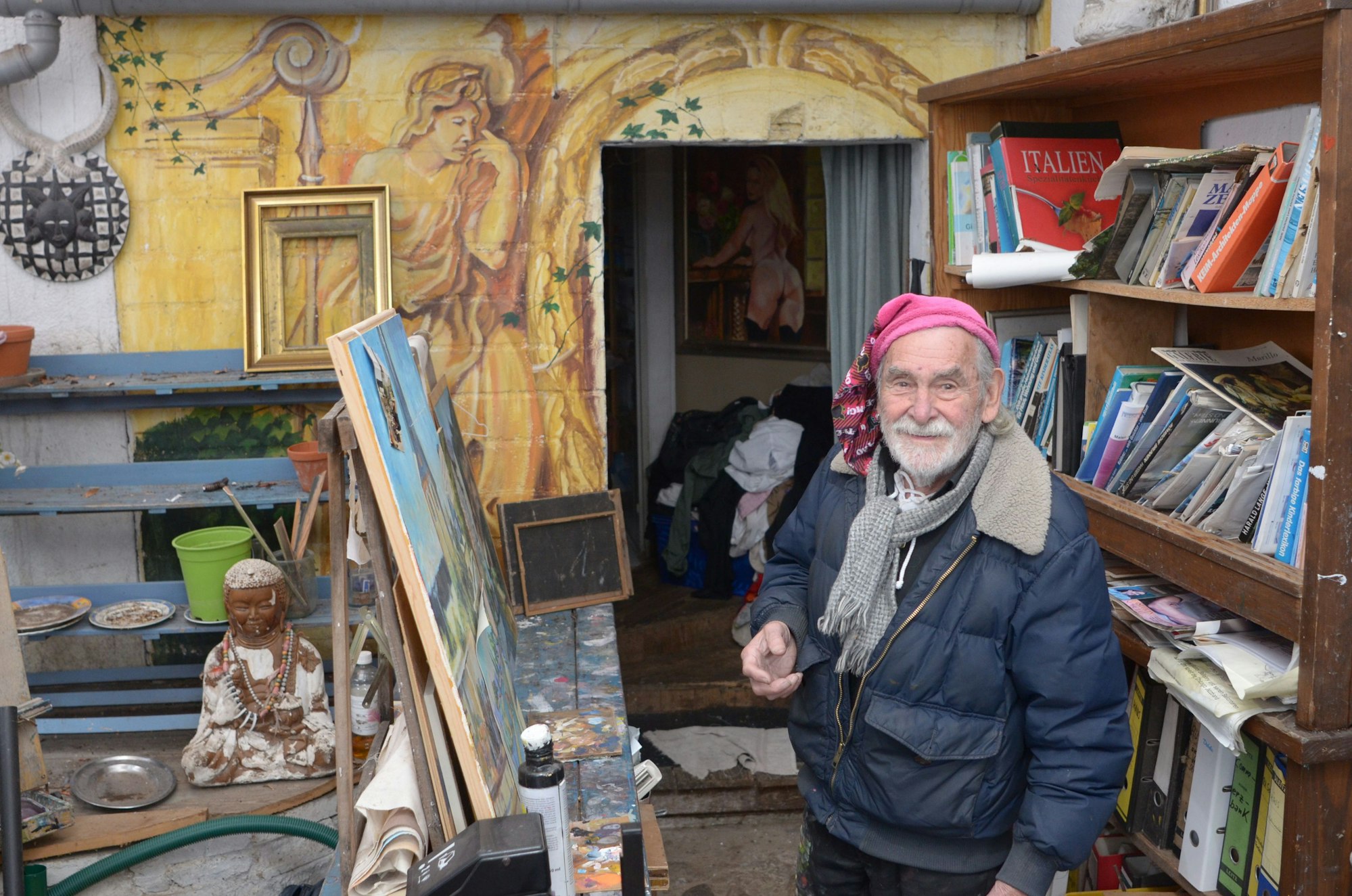 Das Foto zeigt den Maler an einer Staffelei, im Hintergrund eine Wandmalerei.