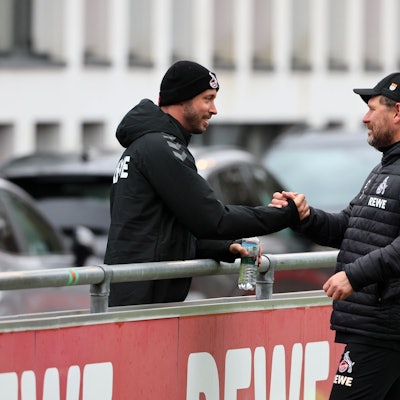 Kölns verletzter Offensivspieler Mark Uth (l.), der eine schwarze Mütze trägt, begrüßt FC-Coach Steffen Baumgart am Rande der Trainingseinheit.