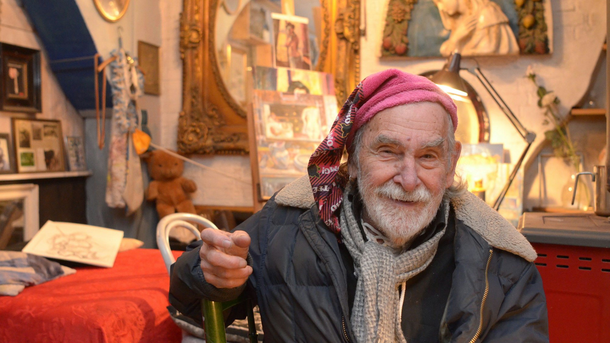 Gus Breuer, mit roter Zipfelmütze und Schal in seiner mit Sammlungsstücken eingerichteten Wohnung.