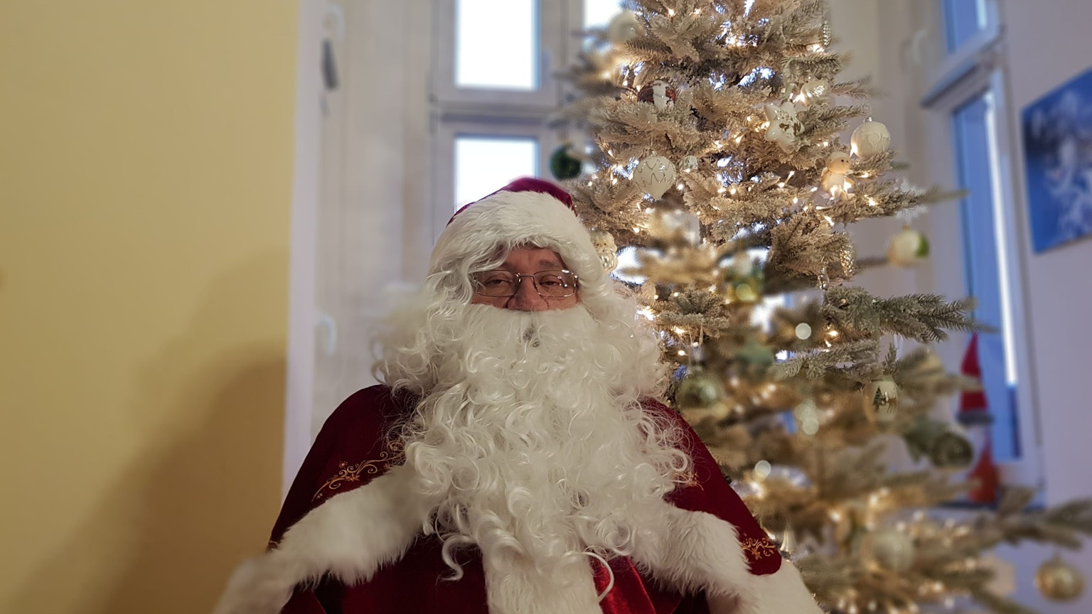 Der Solinger Weihnachtsmann Harald Heidrich sitzt vor dem Weihnachtsbaum in seinem Wohnzimmer.