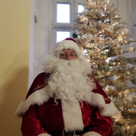 Der Solinger Weihnachtsmann Harald Heidrich sitzt vor dem Weihnachtsbaum in seinem Wohnzimmer.