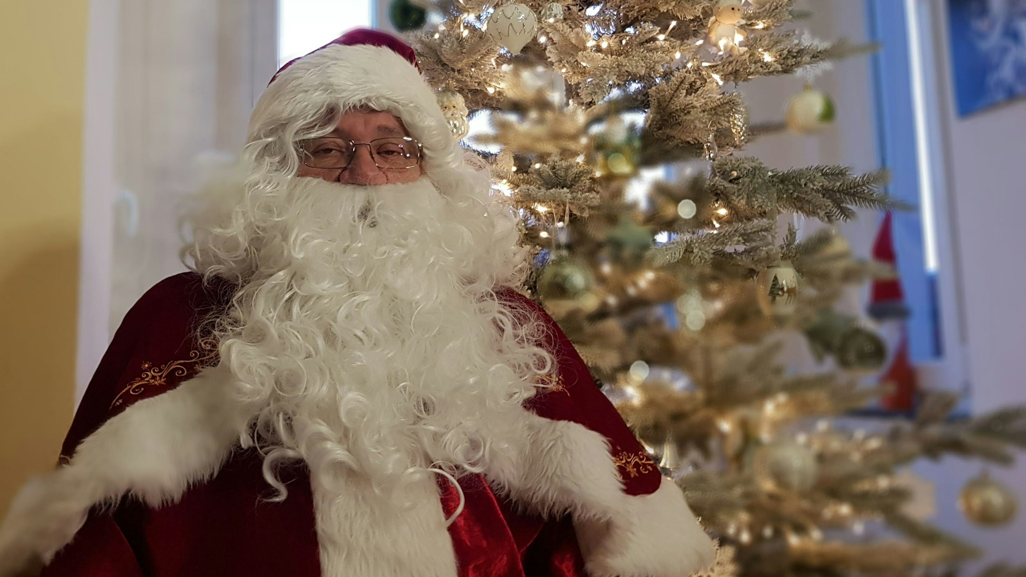 Der Solinger Weihnachtsmann Harald Heidrich sitzt vor dem Weihnachtsbaum in seinem Wohnzimmer.