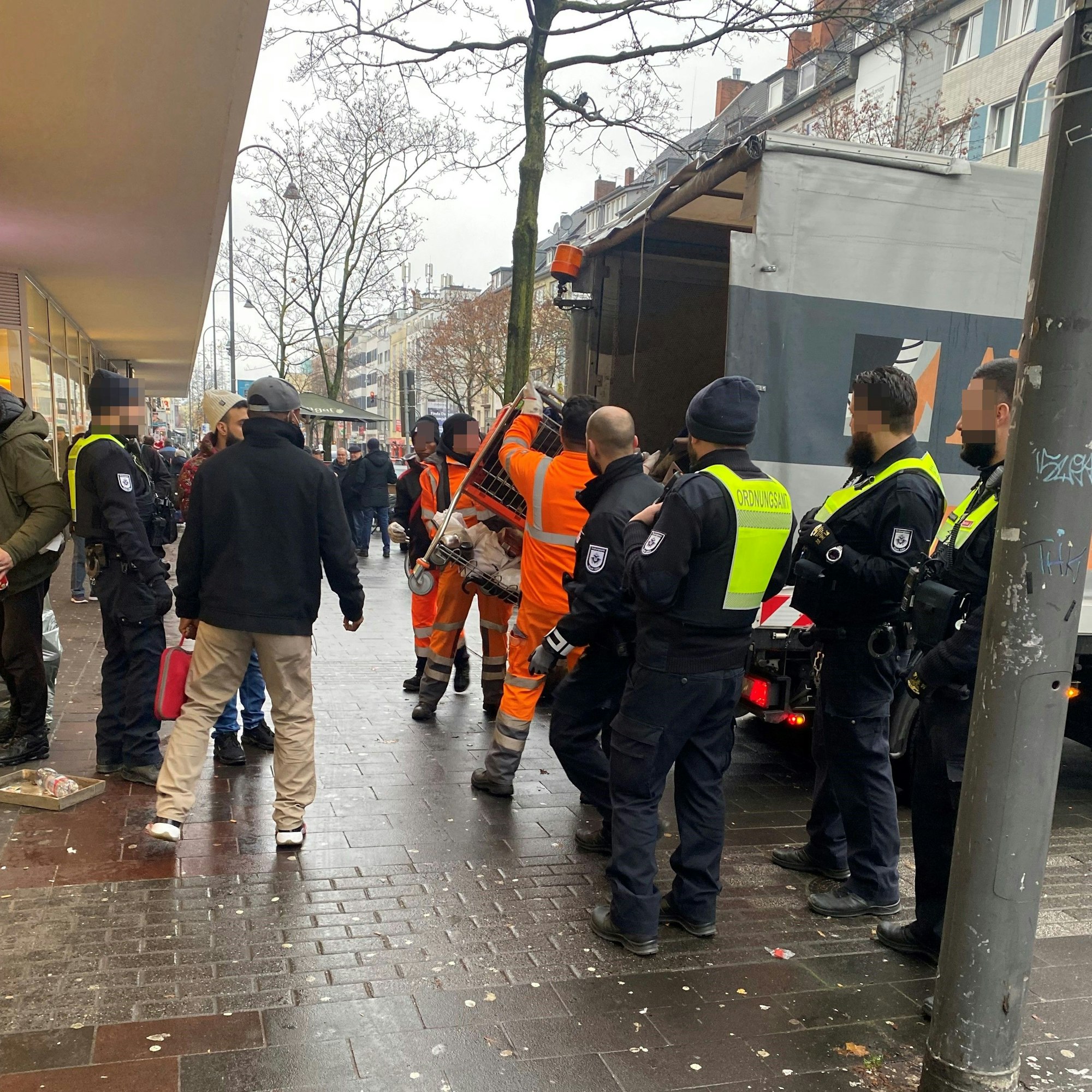 AWB-Mitarbeiter werfen einen Einkaufswagen in den Müllwagen, im Beisein von Ordnungsamtskräften.