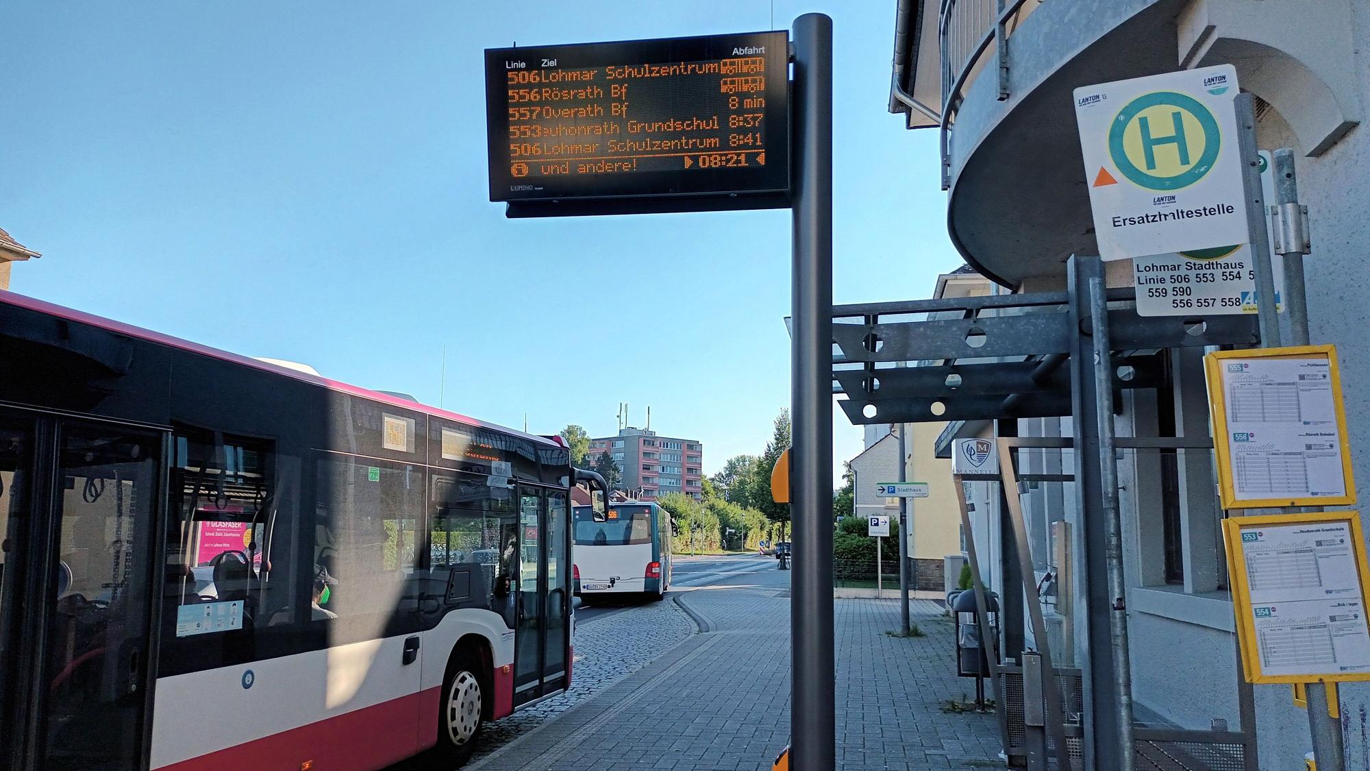 Ein Bus hält an einer Haltestelle. Eine elektronische Anzeige zeigt die Abfahrtezeiten an.
