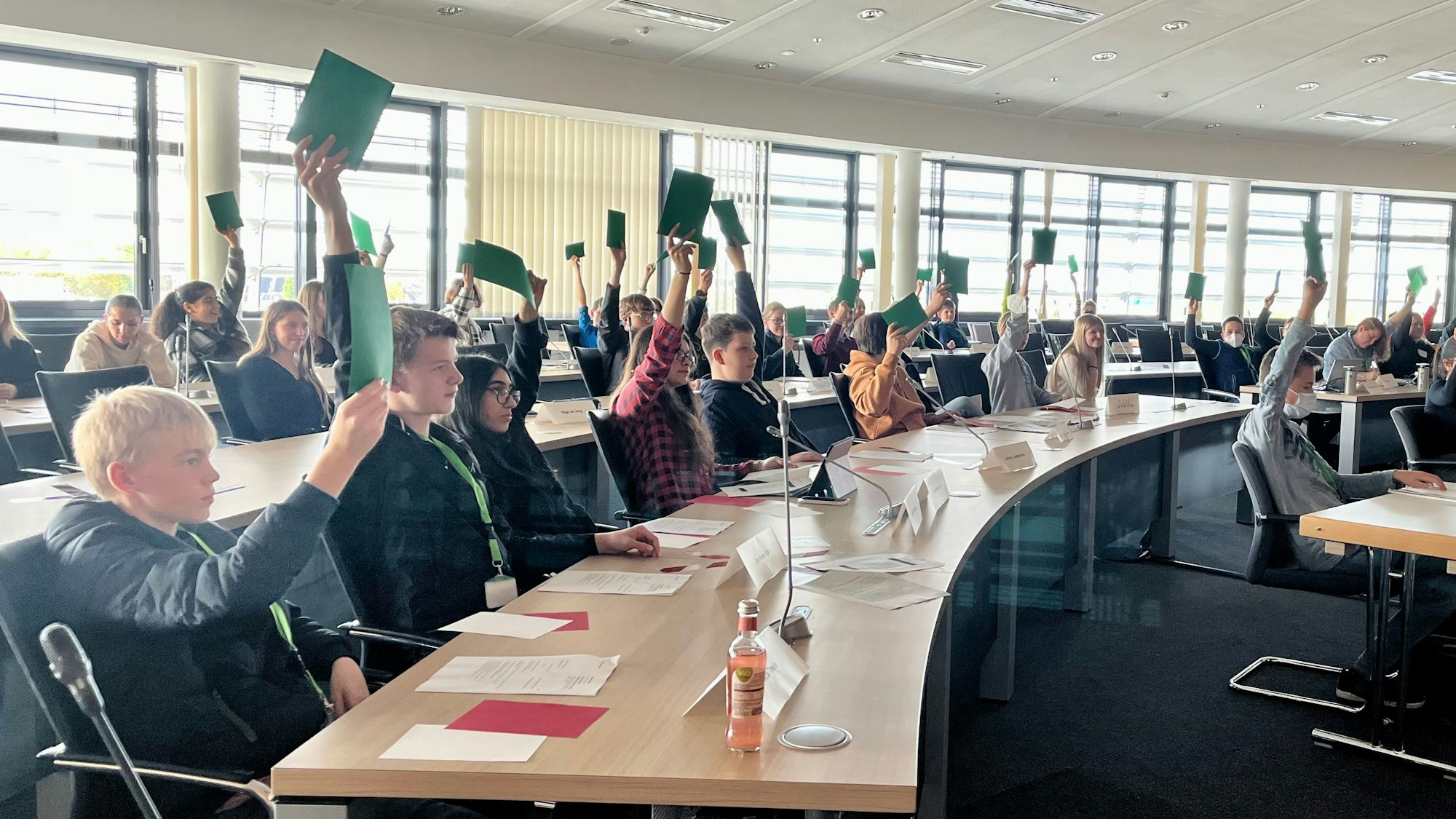 Jugendliche halten im Ratssaal grüne Stimmzettel hoch.