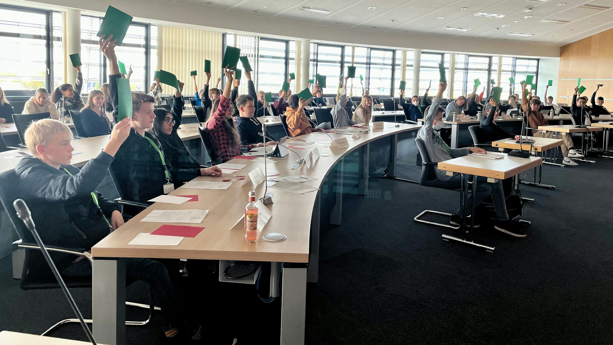 Jugendliche stimmen im Ratssaal mit erhobenen Stimmkarten ab