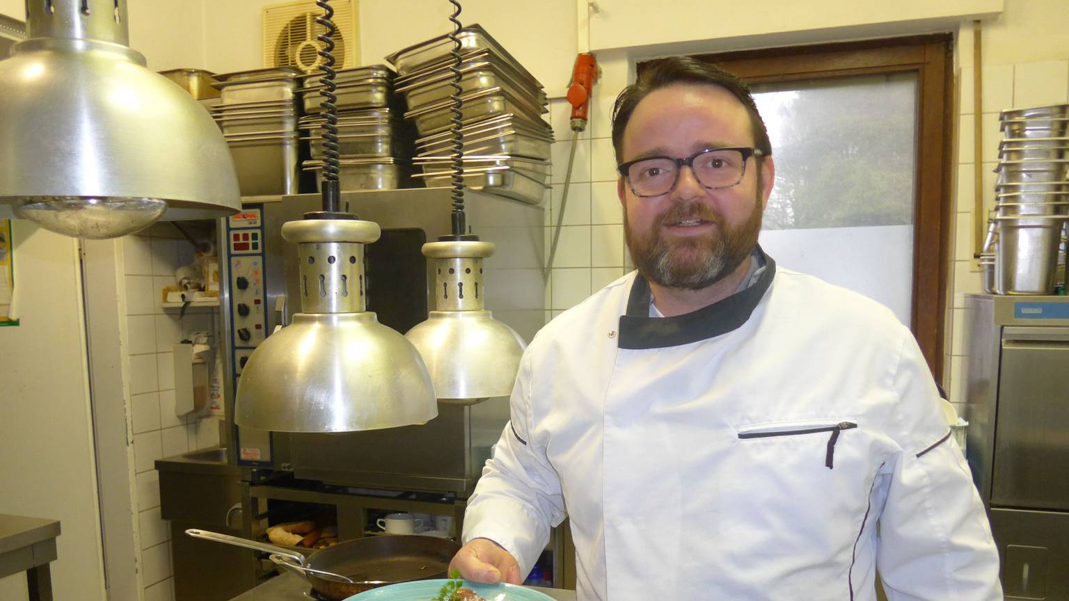 Johannes Richter steht in der Restaurant-Küche und posiert mit einem angerichteten Teller für die Kamera.