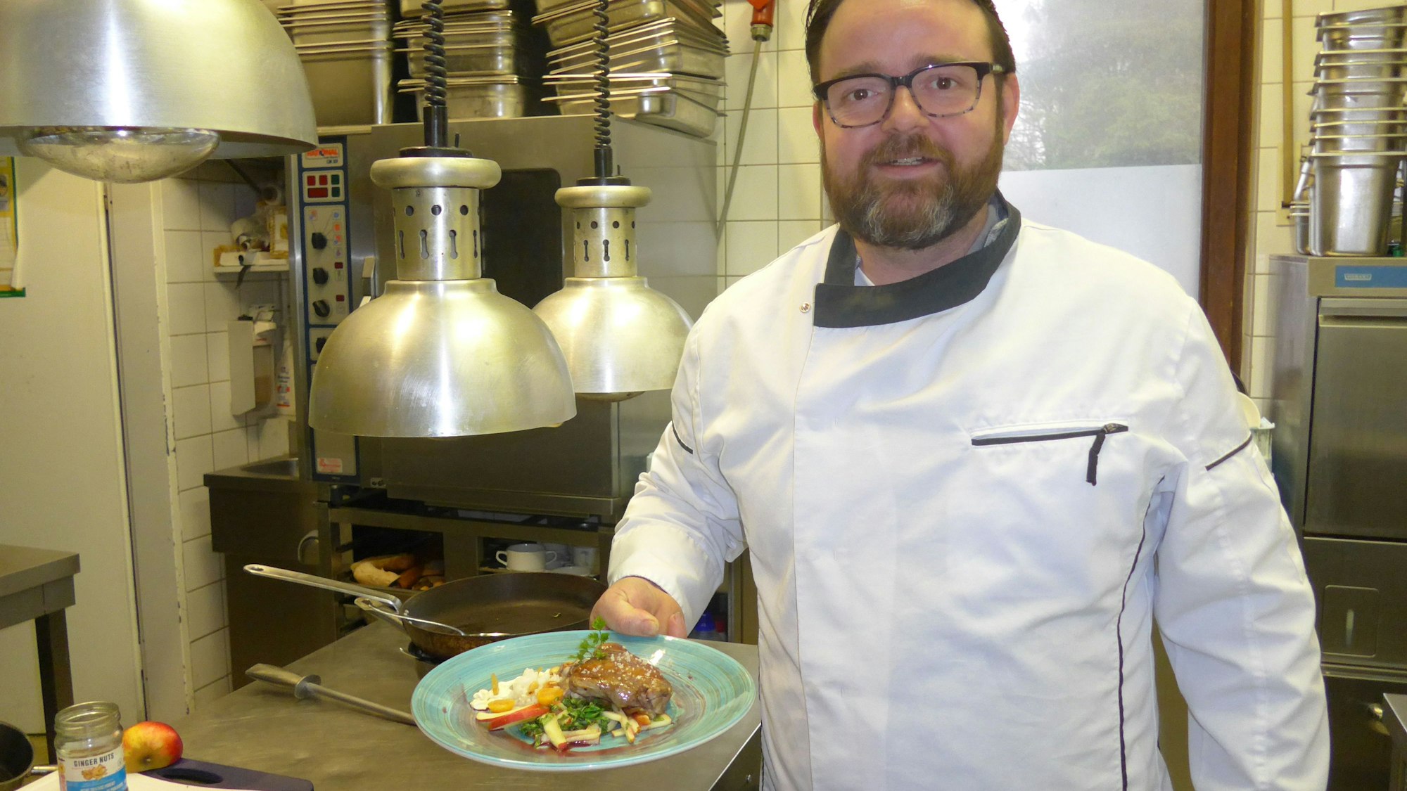 Johannes Richter steht in der Restaurant-Küche und posiert mit einem angerichteten Teller für die Kamera.
