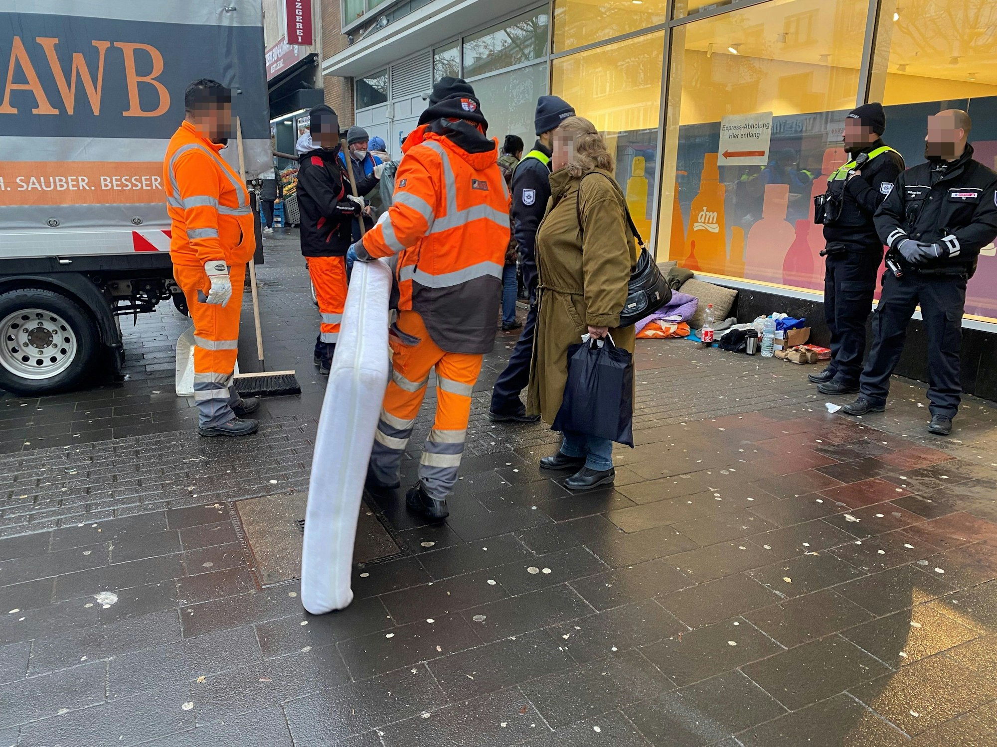 Ein Mitarbeiter der AWB trägt eine Matratze zum Müllwagen, Ordnungsamtsmitarbeiter stehen daneben.