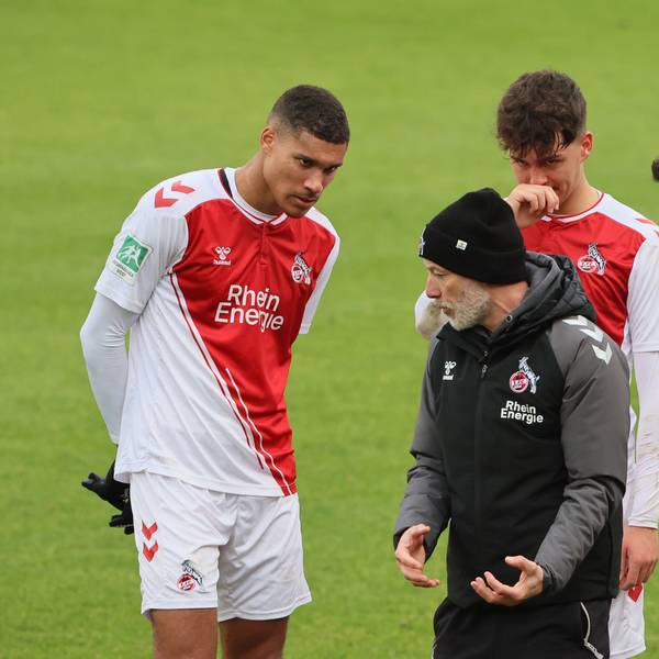 Ein Fußballtrainer steht zwischen dreien seiner Spieler und erklärt ihnen etwas.