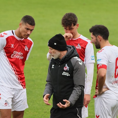 Ein Fußballtrainer steht zwischen dreien seiner Spieler und erklärt ihnen etwas.