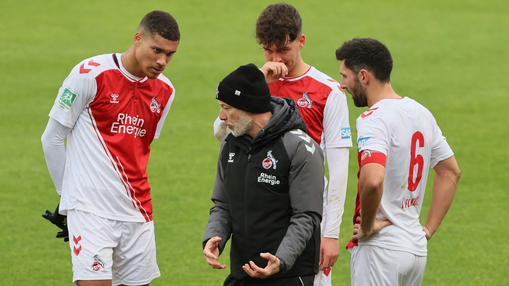 Ein Fußballtrainer steht zwischen dreien seiner Spieler und erklärt ihnen etwas.
