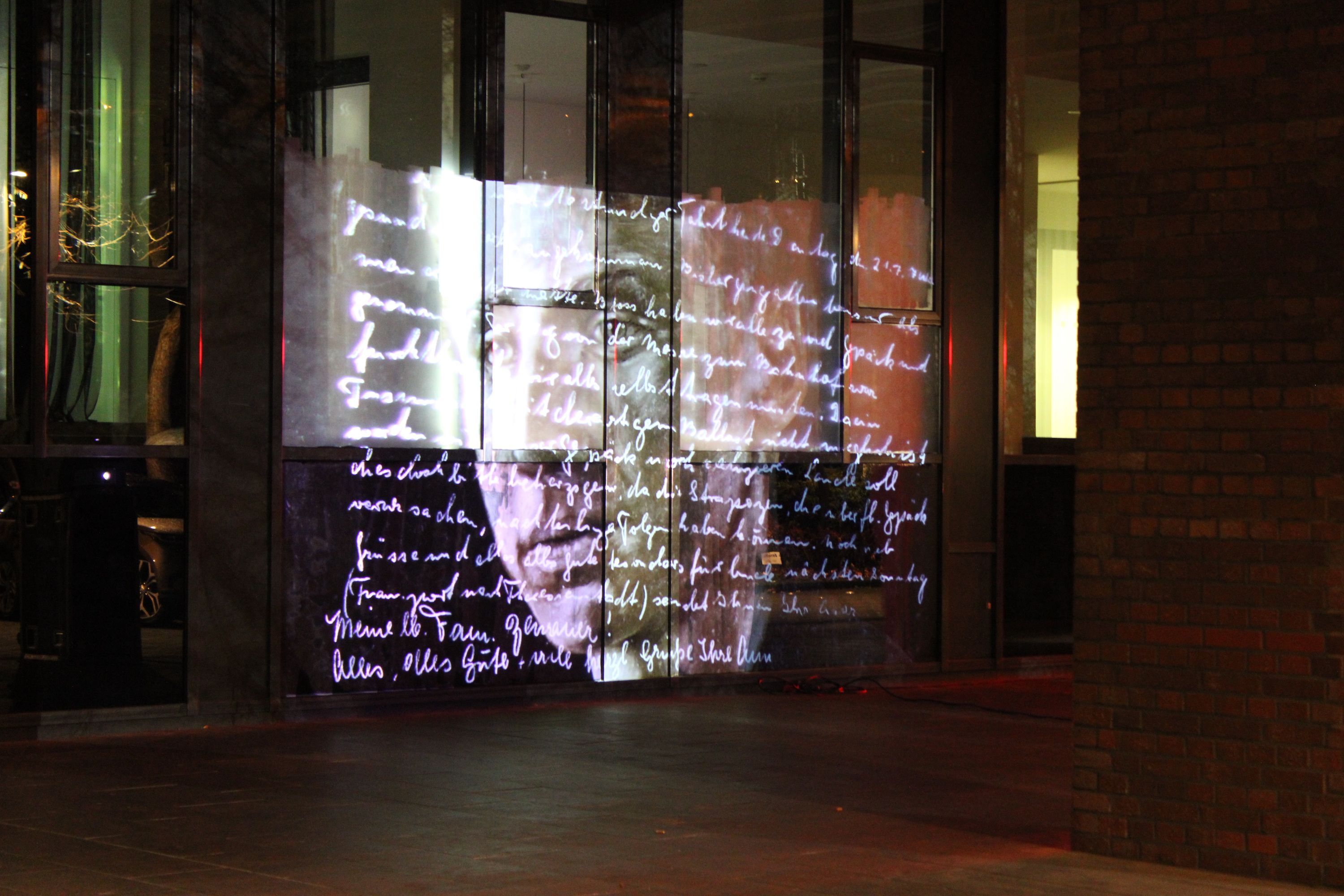 Eine der Projektionen an der Fassade der Kölner Rheinhallen. Ein Opfer des nationalsozialistischen Regimes wird mti einem handschriftlichen Text an eine Fassade projiziert.
