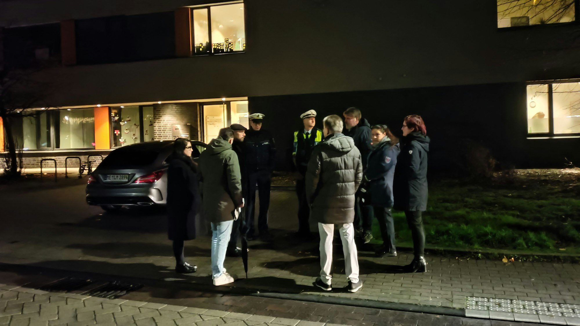 Eine Menschengruppe, darin uniformierte Polizisten, steht vor der Kita an der Hitdorfer Ringstraße, im Gespräch.