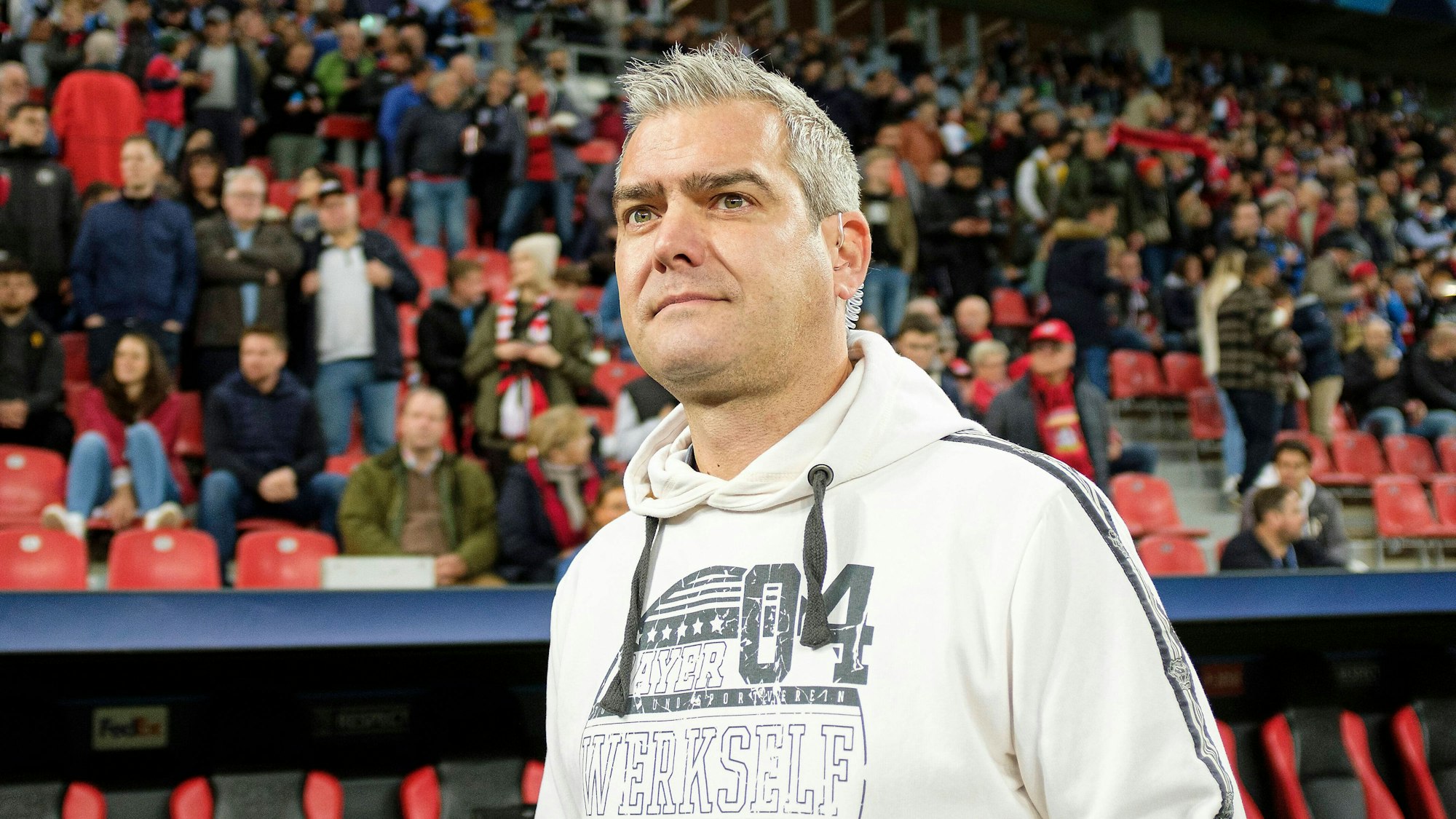 Stadionsprecher Tobias Ufer steht auf dem Spielfeld der Bayarena vor einer Tribüne, auf der Zuschauer sitzen.