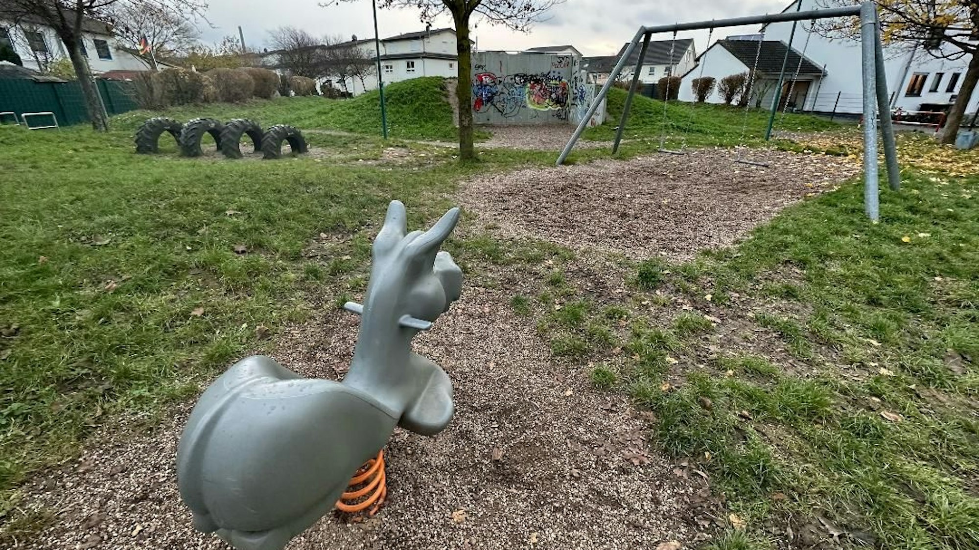 Ein leerer Spielplatz in Niederkassel. Im Vordergrund ist eine Wippe für eine Person, die die Form eines Esels hat. Im Hintergrund sind Schaukeln und Reifen.
