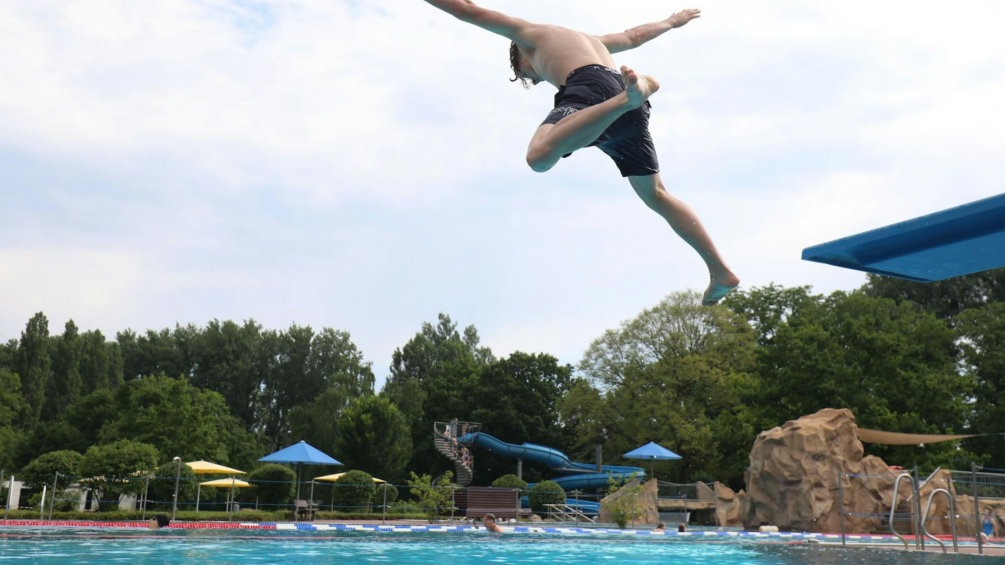 Ein junger Mann springt von einem Sprungbrett ins Becken des Freibades auf Grafenwerth. Im Hintergrund ist eine große Rutsche zu sehen.