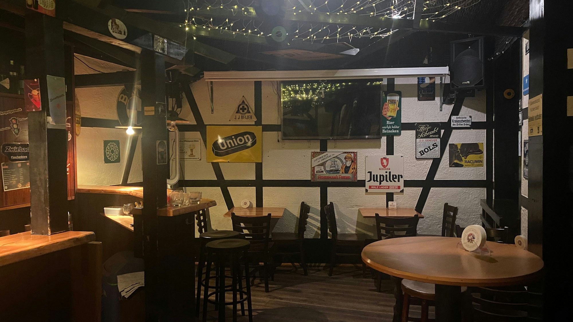 Blick in den leeren Schankraum der Kneipe Zwieback. An einer Wand hängen Bierschilder. Die Wand selbst ist weiß und von braunen Fachwerkbalken durchzogen.