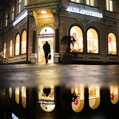 Die Apotheke mit dem Namen «Alte Apotheke» spiegelt sich in einer Pfütze während ein Mann die Apotheke betritt.