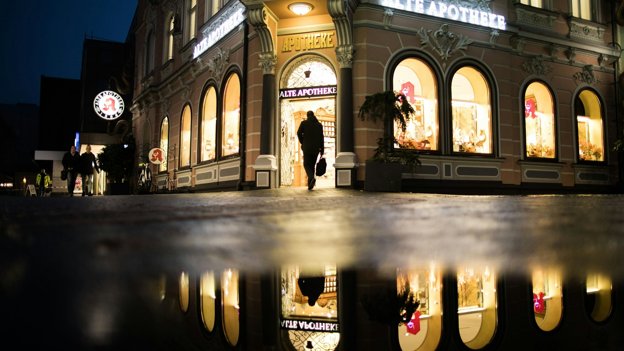 Die Apotheke mit dem Namen «Alte Apotheke» spiegelt sich in einer Pfütze während ein Mann die Apotheke betritt.