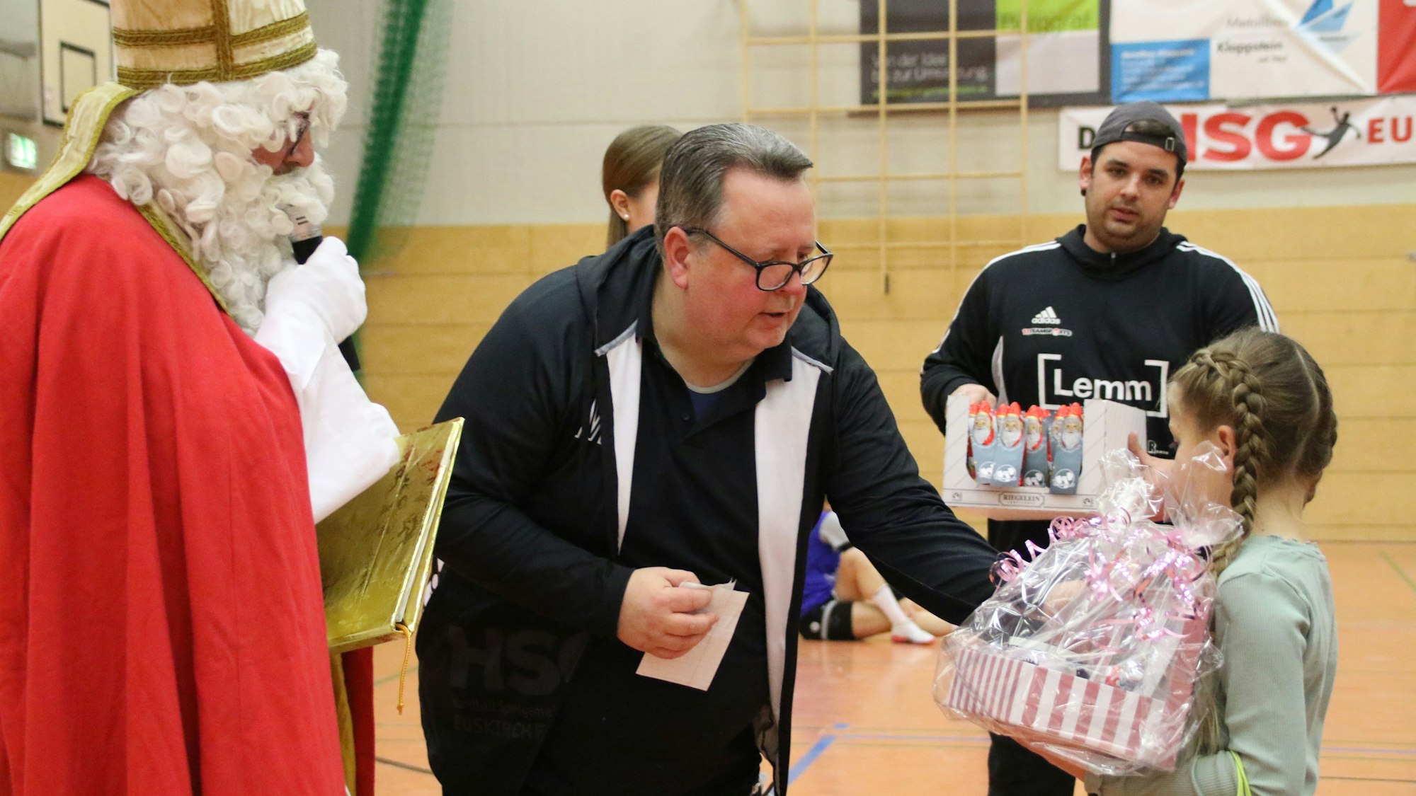 Der Nikolaus und der Vorstand der HSG Euskirchen verteilen an die HSG-Jugend Geschenke. Ein Mädchen mit Zöpfen. hält einen großen Geschenkkorb in seiner Hand.