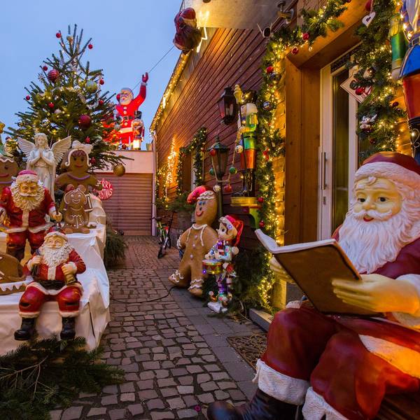Mehrere Weihnachtsmänner, aber auch ein Engel und Lebkuchenfiguren stehen vor einem holzgetäfelten Haus. Auch ein geschmückter Weihnachtsbaum und ein Nikolaus auf einem Garagendach sind zu sehen.