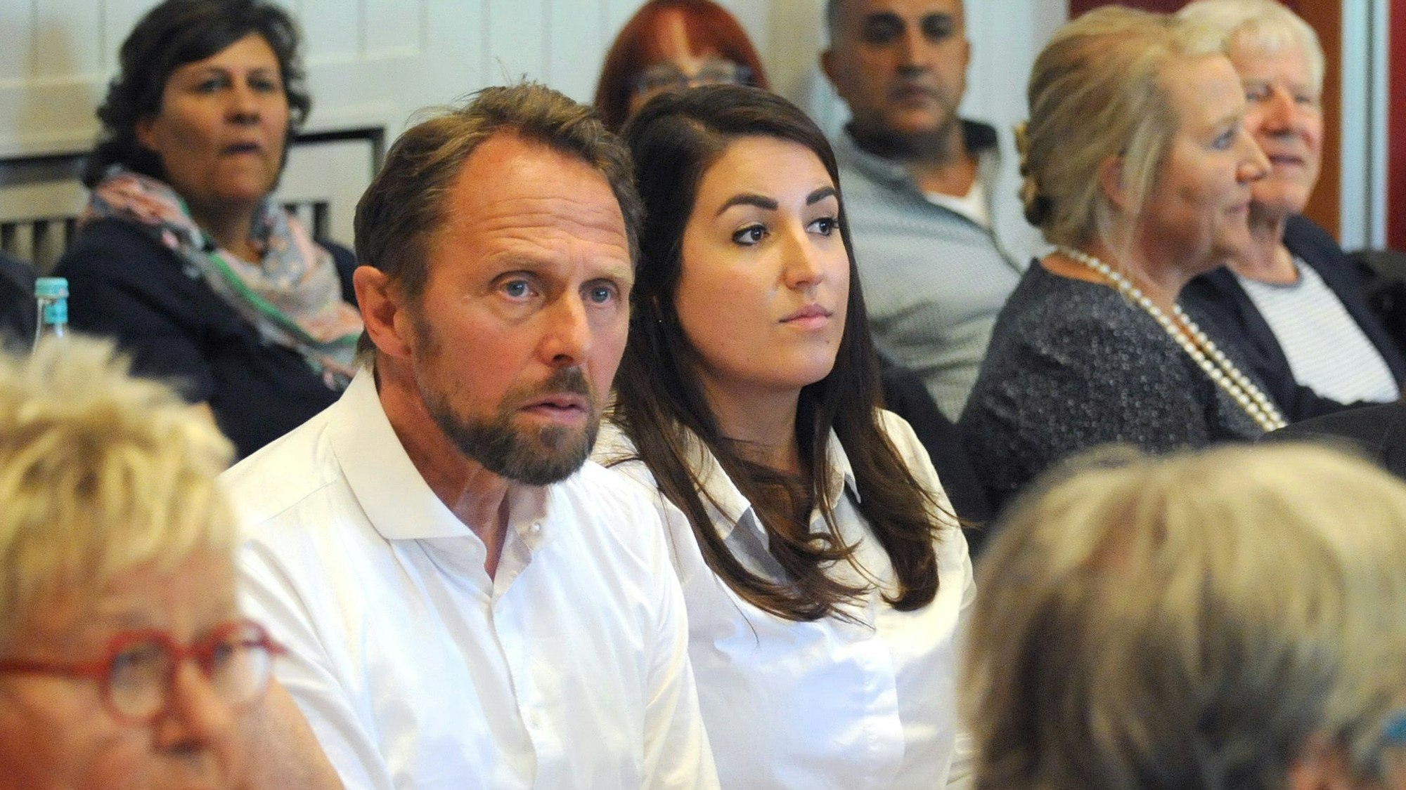 Leverkusens Oberbürgermeister sitzt während einer Veranstaltung neben seiner engsten Vertrauten und Büroleiterin Aylin Doğan. Beide schauen ernst.