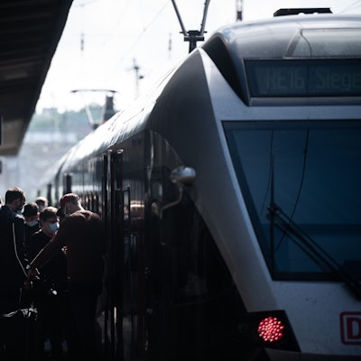 Zu sehen ist ein Zug, der an einem Bahnsteig steht, Menschen drängeln sich beim ein- und aussteigen.