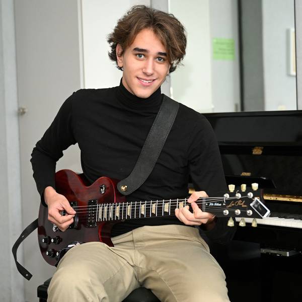 Yves Richter, 19 Jahre alt, sitzt mit einer roten Gitarre in der Hand vor einem Klavier.