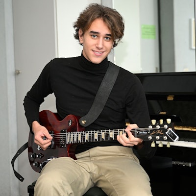 Yves Richter, 19 Jahre alt, sitzt mit einer roten Gitarre in der Hand vor einem Klavier.